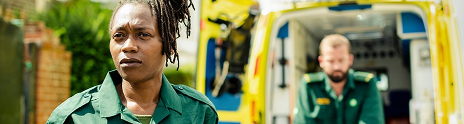 Black lady in paramedic uniform standing in front of an ambulance