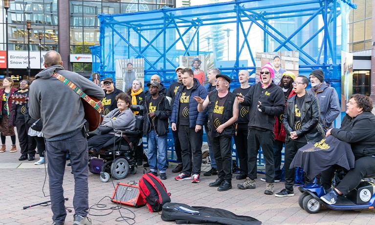 Researcher playing a guitar in front of an audience in a city