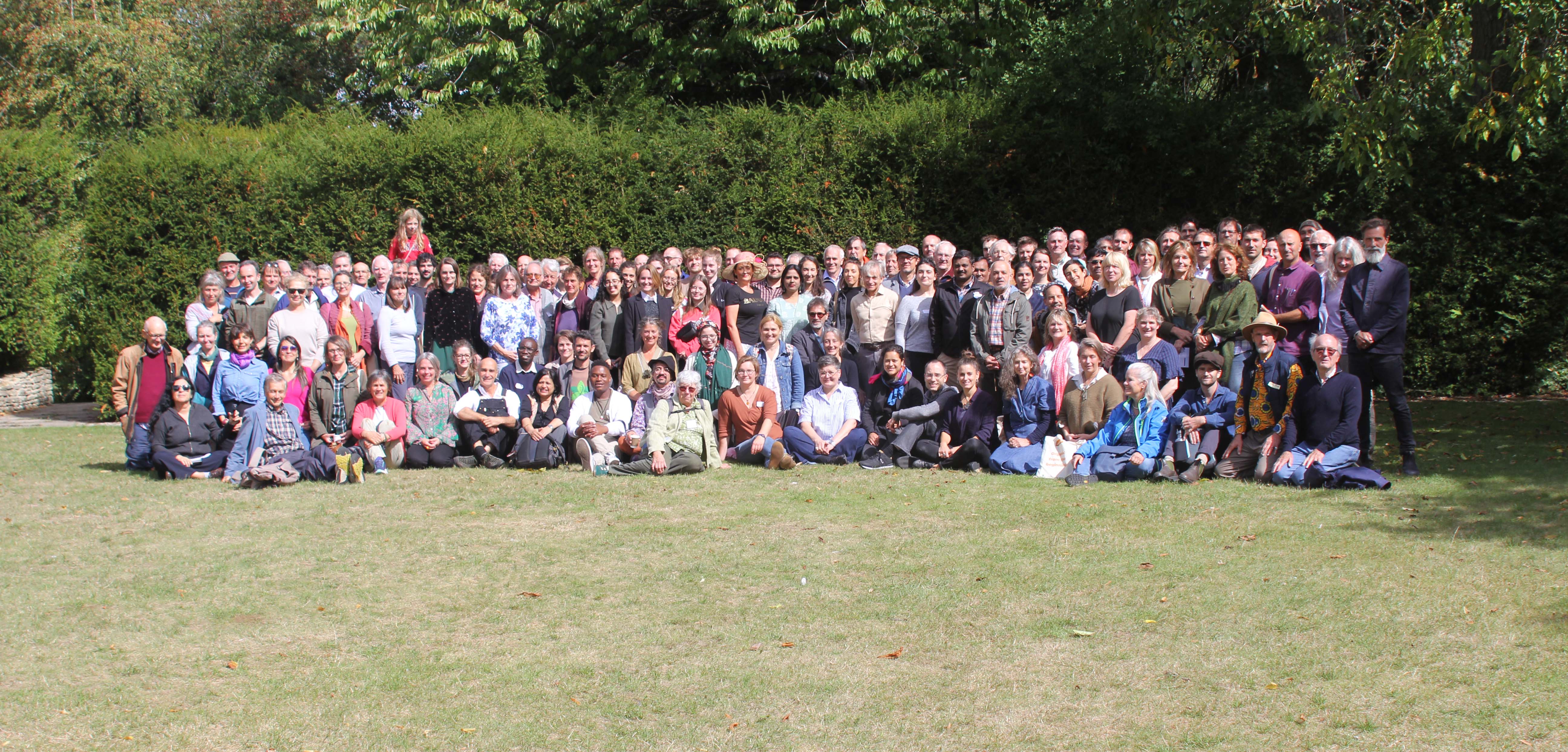 A large group of people grouped for a photo on a grassy area against deeper green hedges