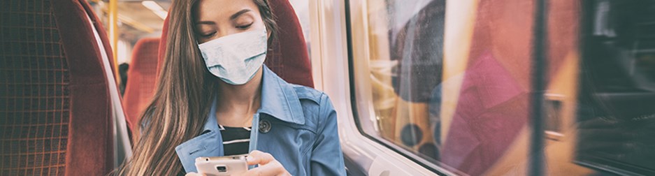 Woman wearing a face mask on a bus while using mobile phone