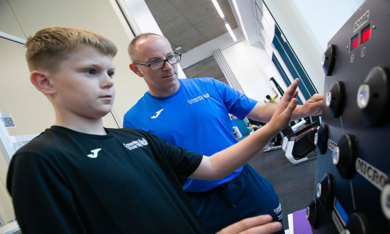 Professor Mike Duncan guiding a child on a piece of sports equipment