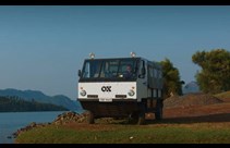 A white truck with OX Delivers branding driving on a dirt track next to a river.