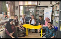 A group of people sat around a yellow table in a room filled with books