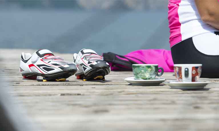 Cyclist shoes and helmet on pavement with coffee cup