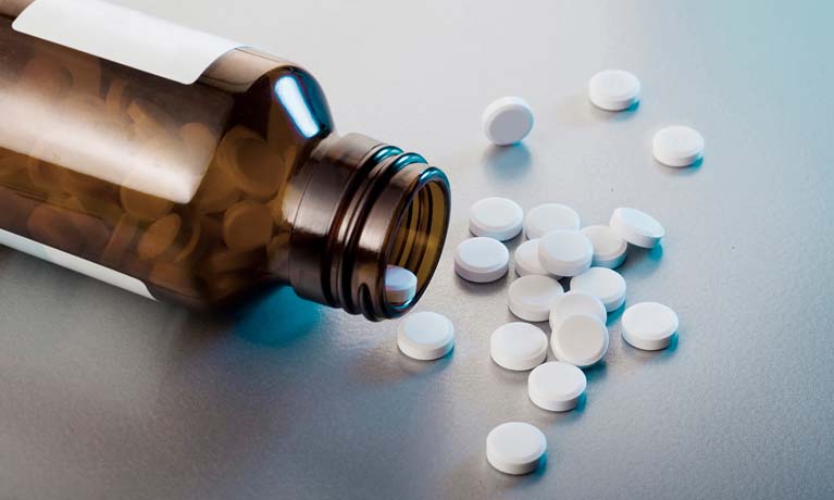 Pill bottle lying on side with pills spilling onto table