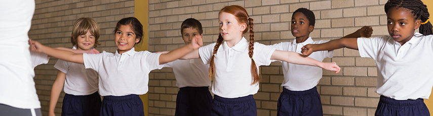 Schoolchildren standing with arms outstretched in PE