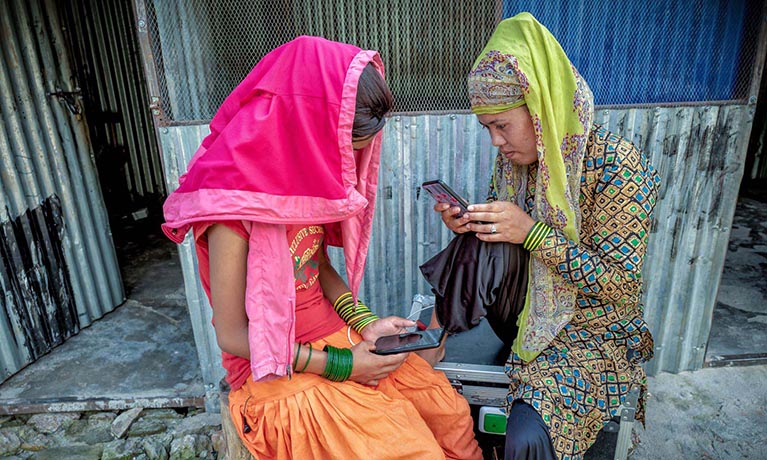 Two females sat together looking at their mobile phone screen.