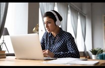 a woman sitting at a laptop wearing headphones