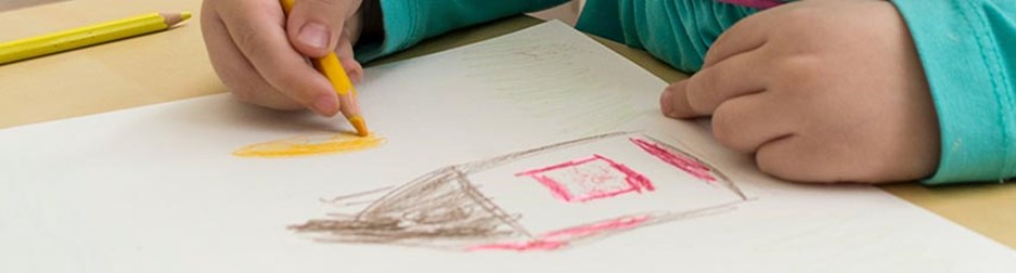 Little girl in a blue dress drawing a house.