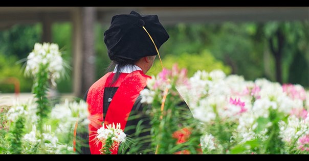a student in a PhD graduation gown in a field