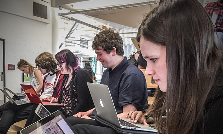 Students sit looking at laptops