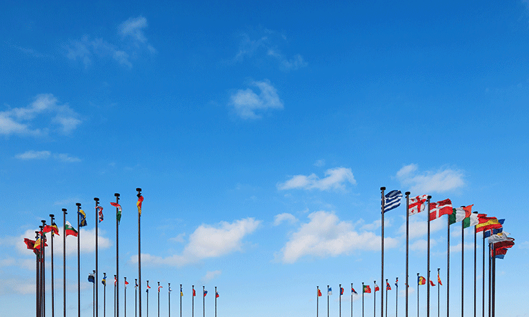 Blue sky with a few clouds, flags of many nations in a circle on tall flagpoles