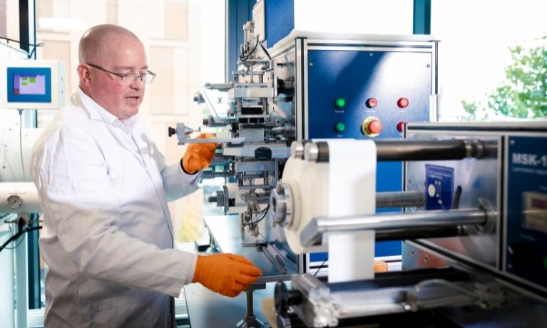 A scientist in a white lab coat and orange gloves using a blue cell prototyping machinectronic cable in orange gloves