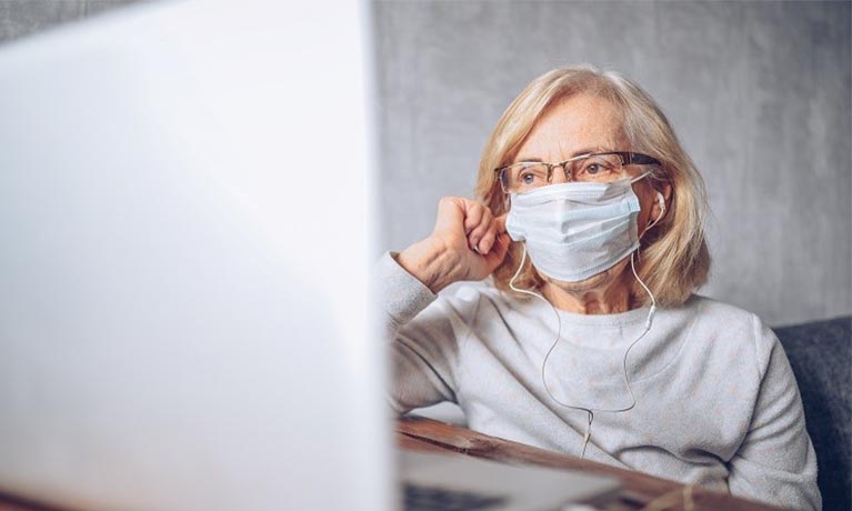 Lady wearing a face mask sat by a computer.