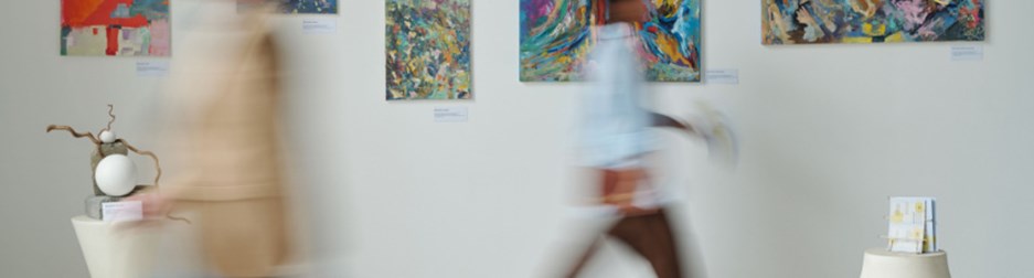 Blurred motion of people passing through the paintings on the wall in art gallery