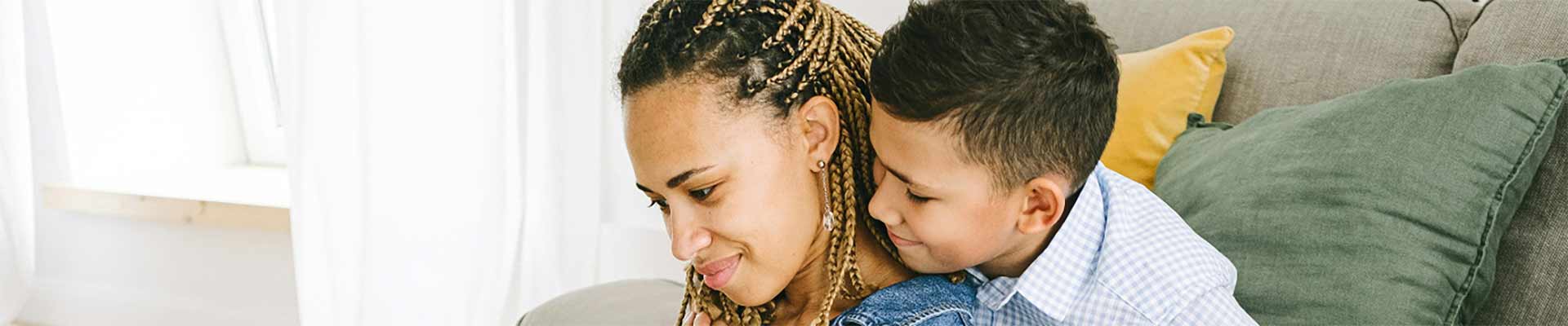 Female looking at a laptop on her laptop her young son has a hand around her neck
