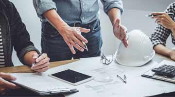 Close up of hands working on construction plans there are plans sitting on the plan