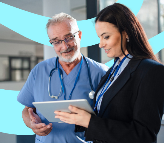 Doctor in blue scrubs and nursing professional in formal attire reviewing a tablet in a hospital setting.