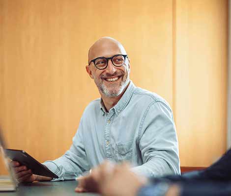 Person in a light blue shirt holding a tablet at a table, with another blurred hand visible in the foreground.