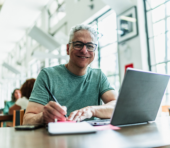 Smiling man working on a laptop and taking notes in a bright, modern workspace.