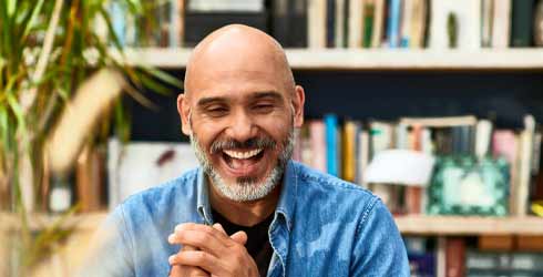 Bald smiling male clasping his hands looking at a laptop screen sitting in a home office