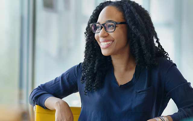 Smiling woman with back curly hair wearing glasses looking to the left