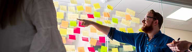 Male lecturer stood in front of a wall of post it notes pointing towards them