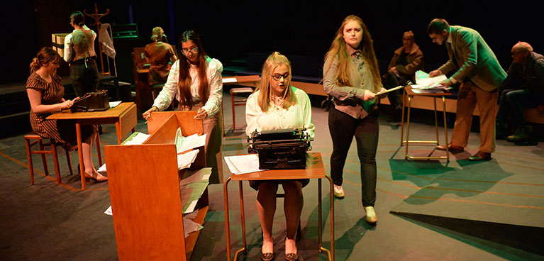 Theatre students on stage with desks and typewriters