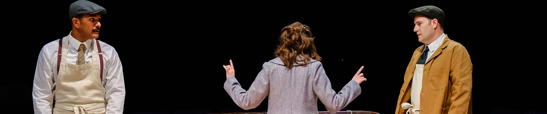 Actors performing on stage in costume with a black backdrop