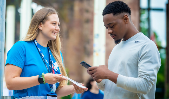 Two students in the cathedral ruins, one wearing a Students' Union uniform and holding a leaflet and the other scanning a code on the leaflet.