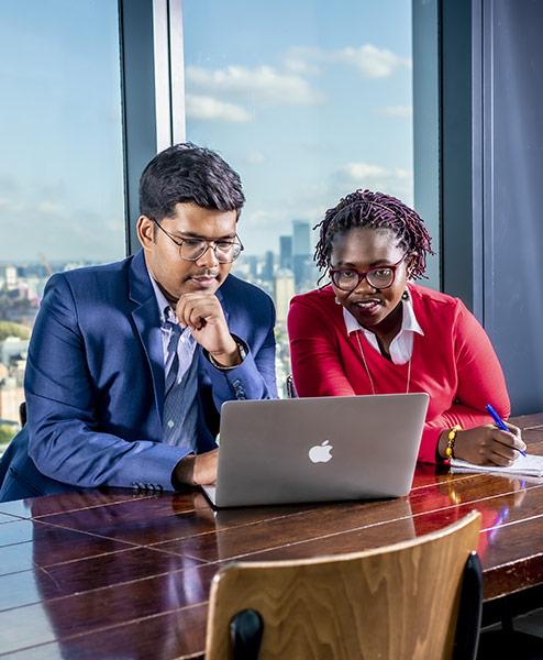 two students looking at a laptop in an office room