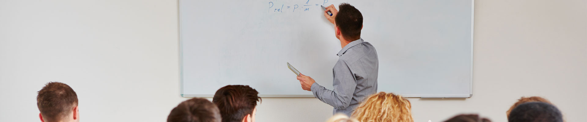 teacher writing on whiteboard in a classroom with students