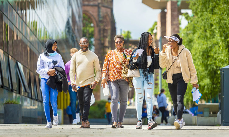 A group of international students walking outside on a sunny day at the Coventry University campus.