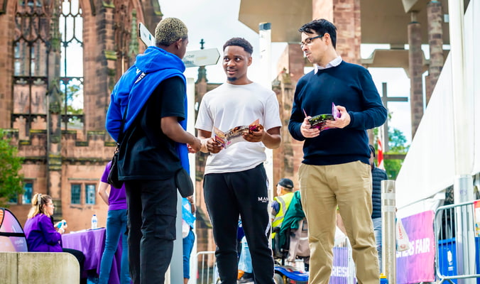 two students and a student advisor standing in the Coventry Cathedral ruins looking at leaflets in conversation