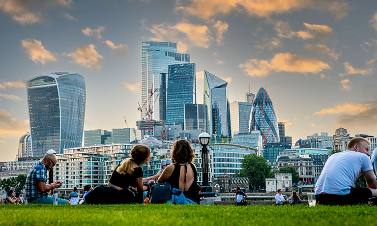 London skyline with iconic buildings in background, people sitting in park in foreground