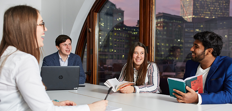 Students sat around a table in front of a window showing a city view