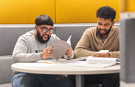 Two smiling students looking at materials while sitting at a booth together