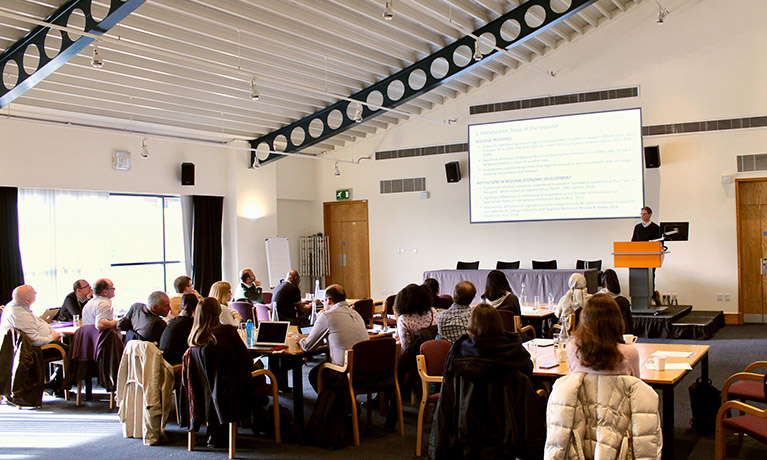 An audience sat at tables in a conference room watching someone give a presentation on stage