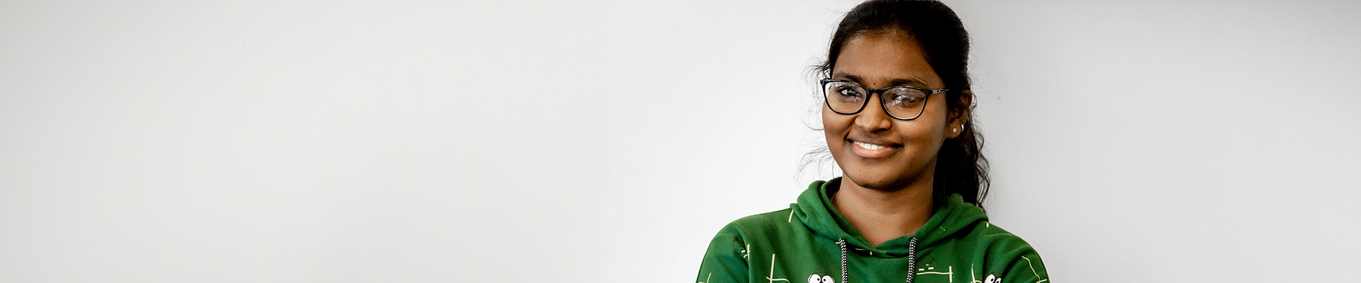 A woman wearing a green jumper with glasses on, smiling at the camera.