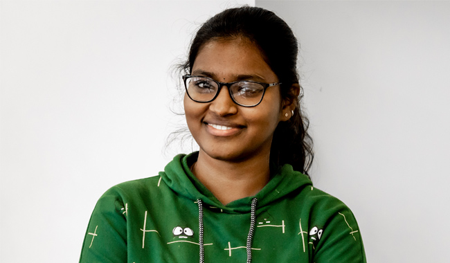 A young woman in a green hoodie smiling at the camera.