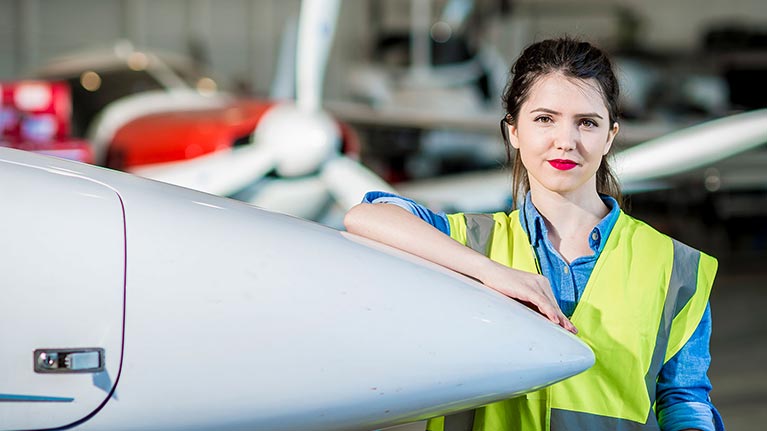 woman in yellow west leaning against a propeller with a plane in a background