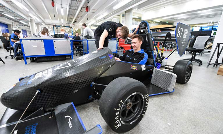 Students working on a motor racing car in an engineering suite