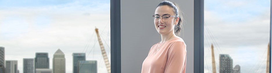 Smiling female student standing next to a window with the London skyline in the background