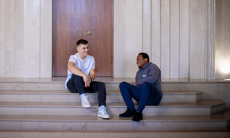 Two students sat on some steps inside a building