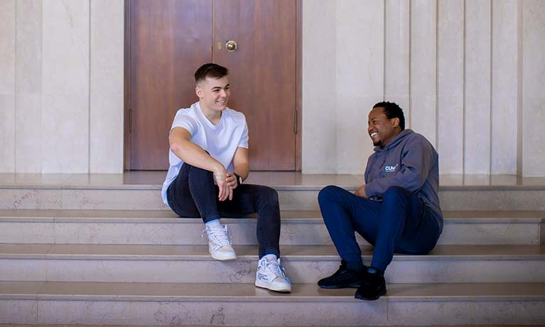 Two male students sat on stairs inside a building talking