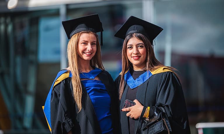 Two female graduates with their graduation gowns and caps
