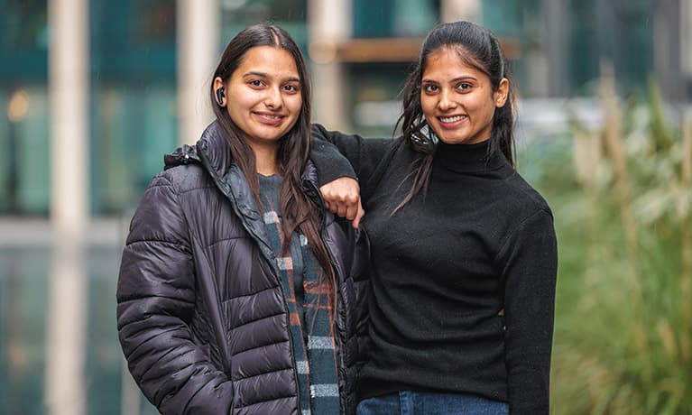 Two students stood outside with one leaning on the other ones shoulder