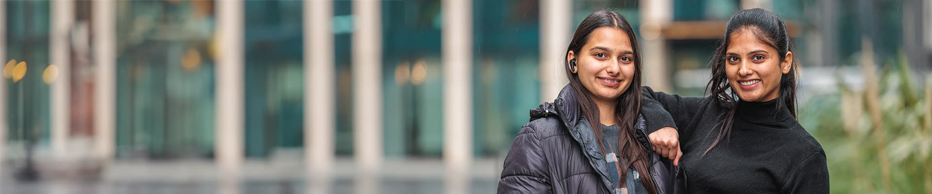 Two female students stood outside smiling at the camera