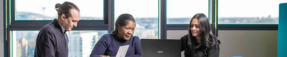 Two students sat around a table with a lecturer looking at their laptops