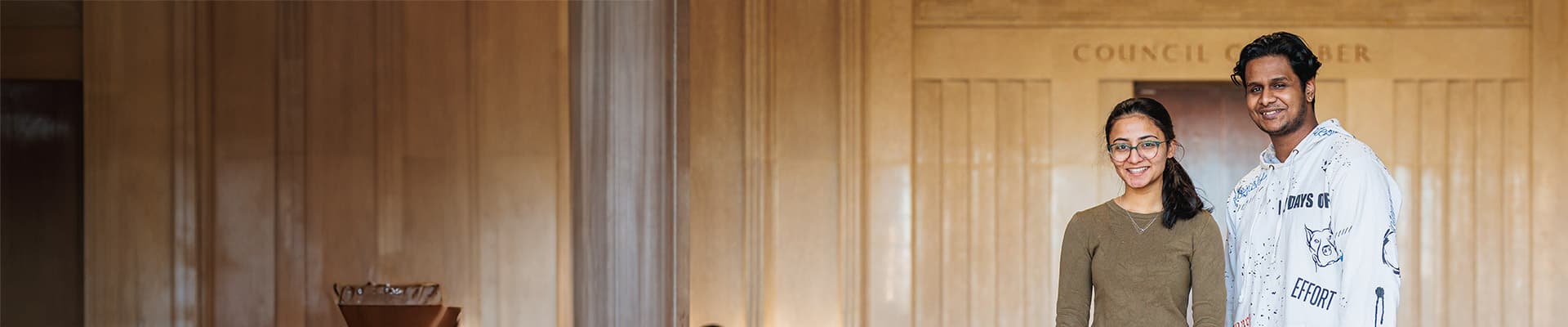 Two students stood indoors smiling